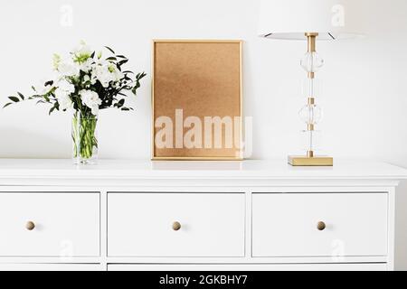 Cornice verticale dorata e bouquet di fiori freschi su mobili bianchi, arredamento di lusso e design per la creazione mockup Foto Stock