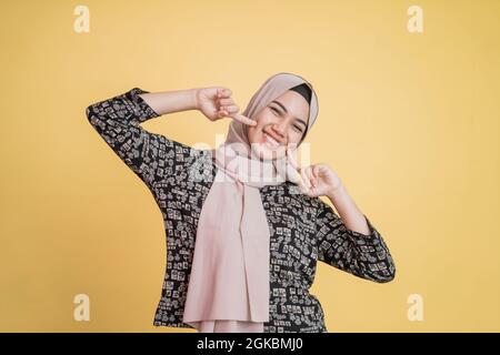 donna hijab musulmana due dita sul mento e sorridente felicemente Foto Stock