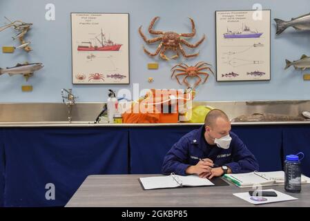 Ufficiale di Petty 2a classe Samuel Chipman, un membro dell'equipaggio della Cutter Stratton della Guardia Costiera, guarda il materiale di addestramento mentre prende le note al centro regionale di addestramento della pesca del Pacifico del Nord (NPRFTC) il 5 marzo 2021, a Kodiak, Alaska. La NPRFTC fornisce istruzioni per far affiorare e far rispettare gli equipaggi delle forze dell'ordine, comandare il personale e sostenere il personale per promuovere la sicurezza marittima, proteggere le risorse preziose e mantenere un terreno di gioco uniforme per la pesca in tutta l'Alaska. Foto Stock