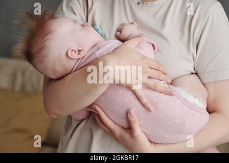 Adorabile bimbo con succhietto in bocca che dorme tranquillamente sulle mani della madre Foto Stock