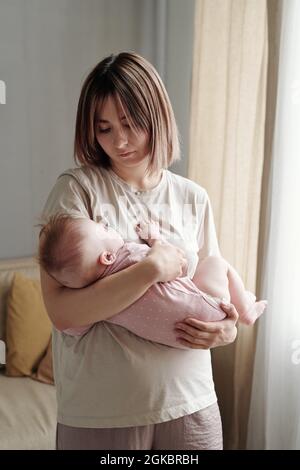 Giovane donna bionda in t-shirt che cullano la sua bambina tranquilla a casa Foto Stock