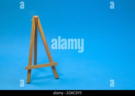 Piccolo cavalletto in legno vuoto su sfondo blu chiaro, da vicino con spazio di copia Foto Stock