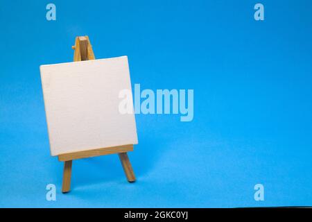 Piccolo cavalletto in legno vuoto su sfondo blu chiaro, da vicino con spazio di copia Foto Stock