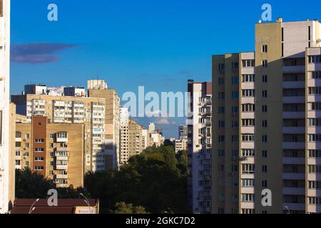 Edifici a più piani contro un cielo blu nelle giornate di sole. Una strada cittadina che si estende fino ad una distanza sepolta da alberi verdi. Mura di alta Unione post sovietica Foto Stock