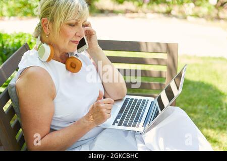 Donna come freelance in giardino sul computer portatile chiama con lo smartphone Foto Stock