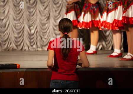 L'insegnante di danza guarda la lezione. La ragazza insegna ai bambini a ballare. Una donna e i suoi studenti. Spettacolo in costumi popolari. Foto Stock