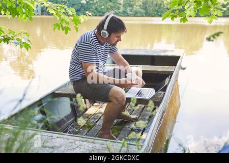 Uomo freelance che utilizza il computer portatile durante la videoconferenza al lago in vacanza estiva Foto Stock