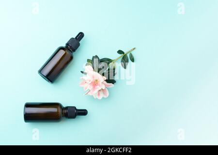 Bottiglie in vetro per siero con pipetta e bellissimo fiore su sfondo verde. Natural Organic Spa concetto cosmetico. Vista frontale. Foto Stock