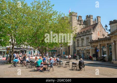 Wells UK, guarda in estate le persone sedute ai tavoli da caffè nello storico Market Place nel centro di Wells, Somerset, Inghilterra, Regno Unito Foto Stock