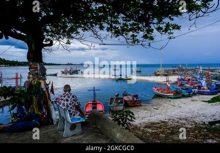 Un anziano uomo tailandese guarda fuori in una piccola insenatura piena di barche da pesca ancorate a Hua Hin, Thailandia Foto Stock