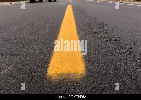 Pista asfaltata appena realizzata con un po' di sporco e la sua consistenza, con una striscia gialla dipinta al centro dell'immagine e sopra l'orizzonte stradale Foto Stock