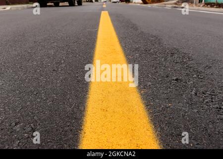 Pista asfaltata appena realizzata con un po' di sporco e la sua consistenza, con una striscia gialla dipinta al centro dell'immagine e sopra l'orizzonte stradale Foto Stock