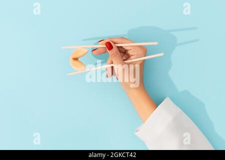 Biscotti di fortuna di tenuta della mano femminile con i chopsticks cinesi su sfondo blu Foto Stock