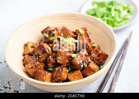 Cubetti di tofu fritti con salsa e semi di sesamo in una ciotola di bambù, vista dal primo piano Foto Stock