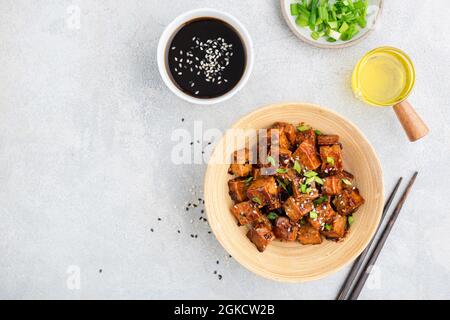 Cubetti di tofu marinati fritti in ciotola di bambù serviti con scallioni tritati, olio di semi di sesamo e salsa di soia. Vista dall'alto dello spazio di copia. Cucina asiatica Foto Stock