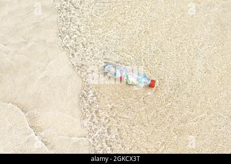 Vista dall'alto di una bottiglia riempita di microplastica sulla riva della spiaggia Foto Stock