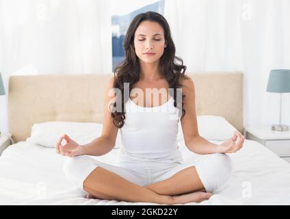 Donna caucasica che pratica yoga e meditating seduta sul letto in casa Foto Stock