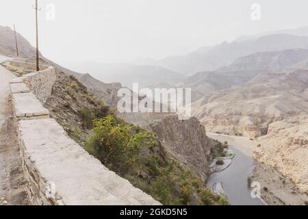 Strati di montagne rocciose e colline nella torbidità del mattino, curva di un fiume in un canyon, vista dall'alto, dalla strada recintata con una recinzione in pietra. In viaggio Foto Stock