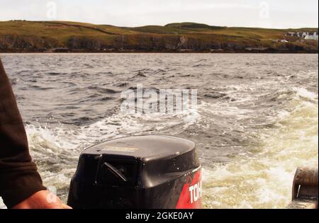 Una vista da un piccolo traghetto passeggeri sulla Kyle of Durness, Scozia guardando indietro mostrando il motore fuoribordo e il braccio e la mano del ferrista Foto Stock