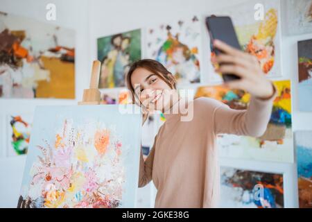 artista femminile asiatica che fotografa il proprio dipinto utilizzando lo smartphone Foto Stock