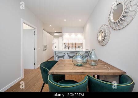 Bel tavolo da pranzo in legno con sedie rivestite in velluto verde, arredamento contemporaneo e cucina isola e moderna cucina sullo sfondo. Marchio Foto Stock