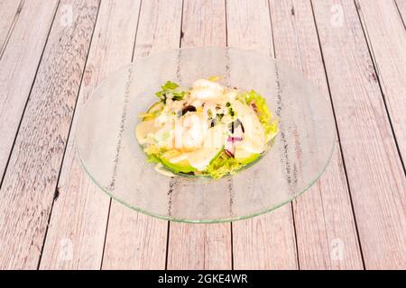 Insalata di gamberi e avocado con lattuga con salsa di panna su vetro trasparente su tavola di legno Foto Stock
