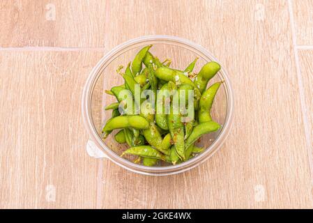 Cialde di edamame con scaglie di sale e salsa calda all'interno di un recipiente di plastica trasparente per la consegna a domicilio Foto Stock