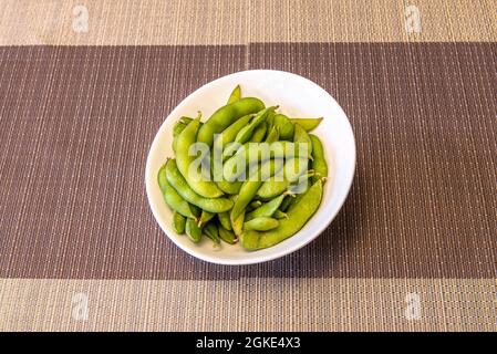 Ciotola bianca con edamame asiatico in cialde su tovaglia di plastica Foto Stock