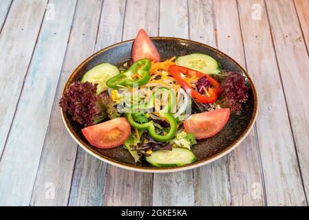 insalata da giardino con germogli di lattuga assortiti, pomodori e cetrioli tritati, fette di cipolla, peperoni verdi e rossi e grani di mais dolce su un bel marrone Foto Stock