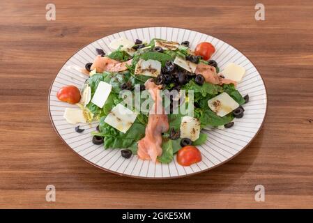 Ottima insalata di spinaci con salmone affumicato, fette di parmigiano, olive nere a fette e olio d'oliva Foto Stock