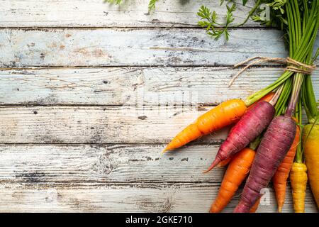Colorata carota arcobaleno con le loro foglie verdi su sfondo di legno, vista dall'alto Foto Stock