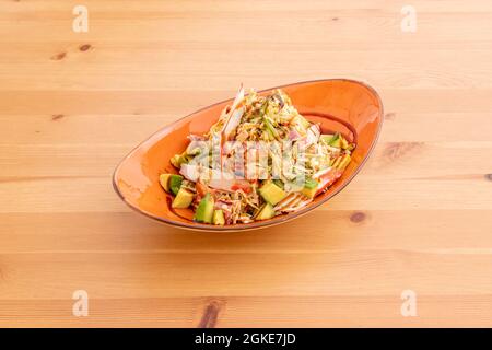 Insalata di pesce con surimi, bonito in scatola, avocado maturi a fette, lattuga iceberg e salsa di soia su tavola di legno Foto Stock