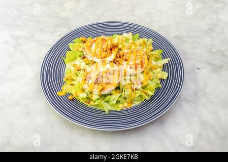Insalata di formaggio di capra con lattuga e noci in una bella piastra bianca a strisce su blu Foto Stock