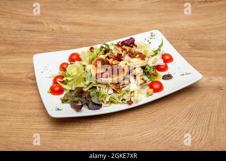 Insalata calda di formaggio di capra con pomodori ciliegini tritati, noci assortite e uvetta con lattuga iceberg Foto Stock