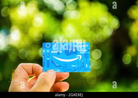 POV mano maschile con nuovo buono regalo Amazon France fr contro il parco verde Foto Stock