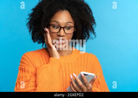 Confuso scioccato Afro donna guardando smartphone leggere cattive notizie, notifica, messaggio sgradevole Foto Stock