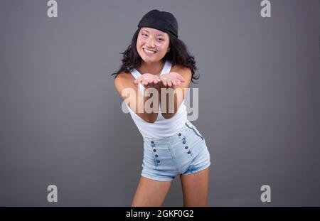 giovane ragazza cinese con bandana, t-shirt e shorts che offrono qualcosa con le mani in avanti Foto Stock