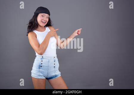 ragazza cinese con bandana e t-shirt isolata che punta a lato mostrando qualcosa. Foto Stock