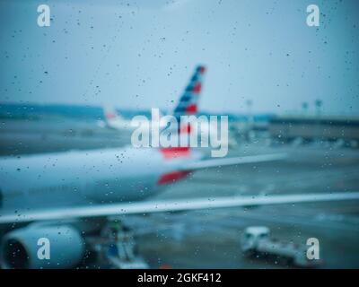 Defocusò l'aereo American Airlines e la pioggia cade sulla finestra all'edificio del terminal dell'aeroporto Foto Stock