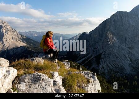 Donna seduta su una roccia in cima alla montagna, godendo di una splendida vista panoramica sulle montagne, Robicje, Alpi Giulie, Slovenia Foto Stock