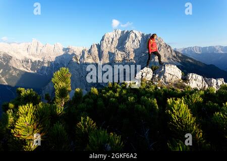 Donna in giacca a vento rossa con uno zaino in piedi due rocce su una cresta di montagna, Robicje, Alpi Giulie, Slovenia Foto Stock