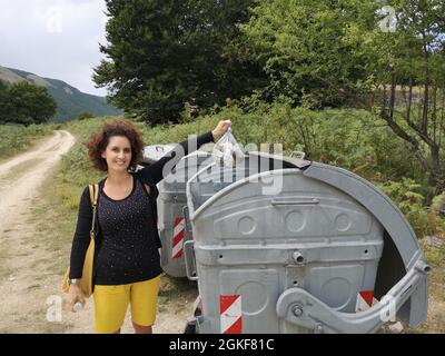 Giovane donna caucasica che getta spazzatura nel polverone in una campagna Foto Stock