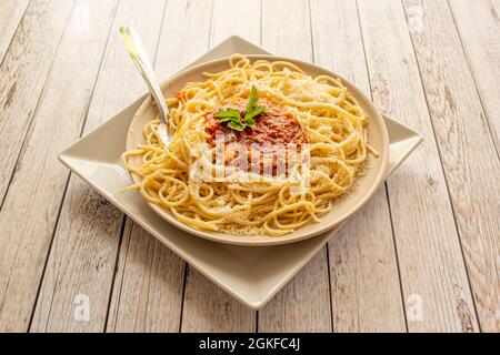 Famosa ricetta italiana per spaghetti con salsa bolognese, parmigiano grattugiato con prezzemolo su un piatto leggero e un tavolo Foto Stock