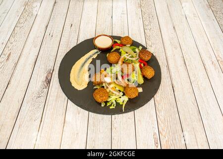 Palline di falafel con insalata di lattuga e cetriolini sottaceto con un piccolo hummus di ceci su un piatto di ardesia nera Foto Stock