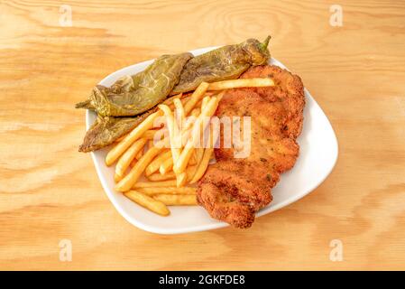 filetto di manzo in pastella con pangrattato, uovo e prezzemolo guarnito con patatine fritte e peperoni verdi fritti su tavola di legno Foto Stock