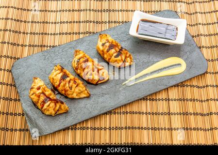 Vassoio grigio con porzione di gnocchi cinesi fritti, dim sum, salsa con soia e crema di patate su una tovaglia di bambù Foto Stock