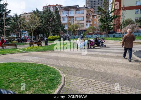 Maltepe, Istanbul, Turchia - 04.13.2021: Un vecchio uomo turco a piedi e alcune donne con maschere protettive seduta nel parco pubblico in quarantena restriti Foto Stock