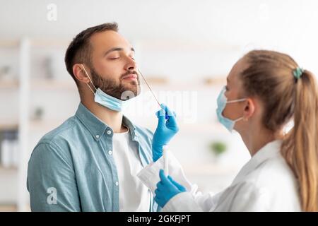 Medico femminile che fa il test PCR del coronavirus nasale per il ragazzo millenario in clinica. Concetto di protezione delle malattie infettive Foto Stock