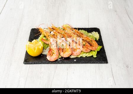 Grande porzione di gamberi fritti da Cadice sul grill e inviare su un letto di lattuga, con succo di limone, prezzemolo tritato e scaglie di sale su un ardesia nera Foto Stock