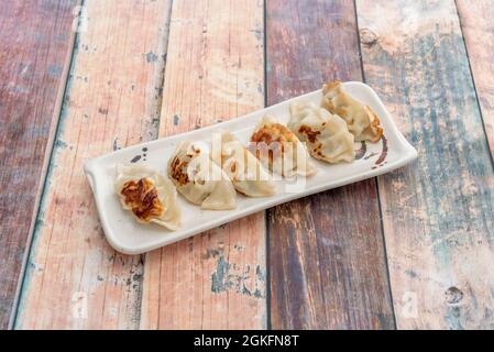 Razione di gnocchi giapponesi, gyozas, fritto alla griglia farcito di carne su tavola di legno Foto Stock